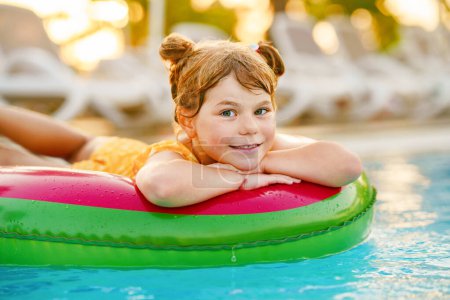 Foto de Niña feliz con anillo de juguete inflable flotar en la piscina. Pequeño niño preescolar aprendiendo a nadar y bucear en la piscina al aire libre del complejo hotelero. Actividad deportiva saludable y diversión para niños - Imagen libre de derechos