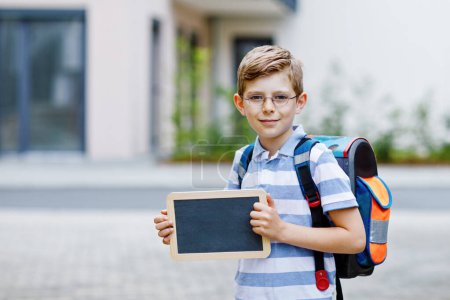 Photo for Happy little kid boy with backpack or satchel. Schoolkid on the way to school. Healthy adorable child outdoors With chalk desk for copyspace. Back to school or schools out - Royalty Free Image