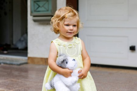 Foto de Pequeña niña jugando con un perro de juguete suave. Lindo bebé niño sosteniendo juguete y juega al aire libre - Imagen libre de derechos