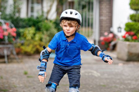 Portrait of little school kid boy in safety protection clothes scating with rollers. Active sporty child doing sports on summer day. Outdoor activity for kids
