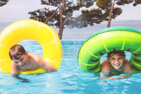 Téléchargez les photos : Deux enfants garçons s'amusent sur des anneaux gonflables en caoutchouc dans la piscine extérieure. Vacances d'été. Week-end d'été pour enfants. Enfants qui s'amusent, frères en vacances en famille - en image libre de droit