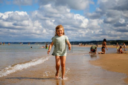 Photo for Happy preschool girl having fun on the sand beach Omaha at Atlantic coast of Normandy, France. Outdoor summer activities for kids. - Royalty Free Image