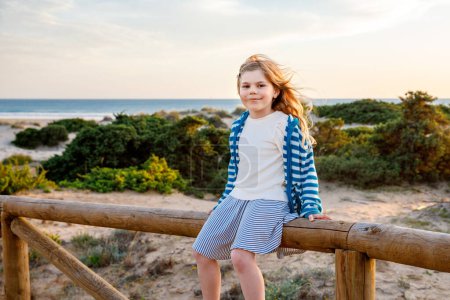 Photo for Adorable happy smiling little girl on beach vacation at sunset. Handsome cute preschool child with long blond hairs having fun on family vacations - Royalty Free Image