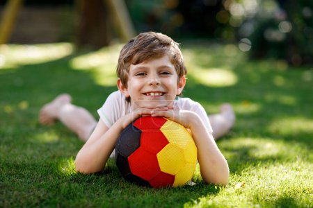 Happy active kid boy playing soccer with ball in German flag colors. Healthy child having fun with football game and action outdoors.