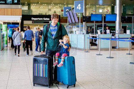 Photo for Cute little toddler girl and father at the airport. Happy family traveling by plane, making vacations. Young dad and baby daughter with suitcases waiting for flight. Family going on journey. Ireland. - Royalty Free Image