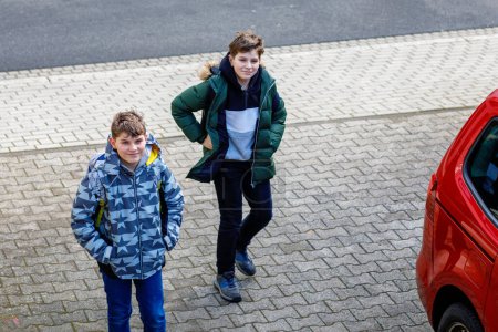 Photo for Two happy school students walking on street after school and chatting. Teenager boys, brothers and friends. Portrait of joyful young boys pupils with backpacks in good mood speaking outdoors in city - Royalty Free Image