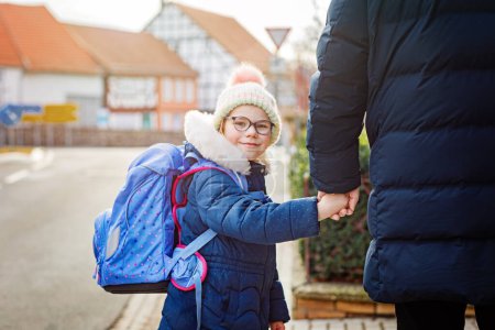 Photo for Little girl and middle aged dad on the way to elementary school. Father holding daughter, school child by hand. Happy family on the street, back to school - Royalty Free Image