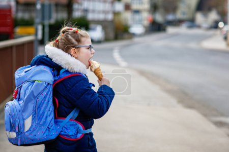 Photo for Cute little girl o the way home from school. Healthy happy child with eyeglasses with ice cream cone. Smiling child with schoolbag and icecream on the city street, outdoors - Royalty Free Image