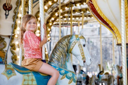Photo for Happy positive preschool girl having a ride on the old vintage merry-go-round in city of St Malo France. Smiling child on a horse - Royalty Free Image