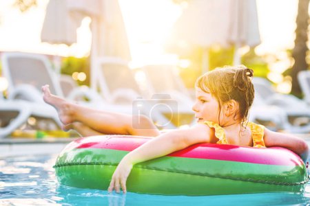 Téléchargez les photos : Bonne petite fille avec flotteur anneau gonflable dans la piscine. Petit enfant d'âge préscolaire apprenant à nager et plonger dans la piscine extérieure de la station hôtelière. Activité sportive saine et plaisir pour les enfants - en image libre de droit