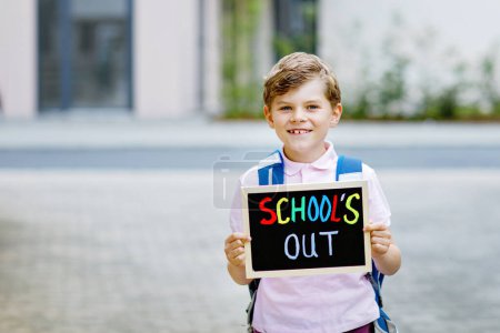 Happy little kid boy with backpack or satchel. Schoolkid on the way to school. Healthy adorable child outdoors With chalk desk for copyspace. Back to school or schools out