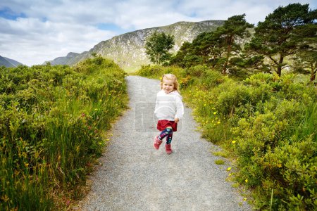 Nettes kleines, glückliches Kleinkind, das auf einem Naturpfad im Glenveagh Nationalpark in Irland läuft. Lächelndes und lachendes Baby, das seinen Familienurlaub in der Natur genießt. Reisen mit kleinen Kindern.