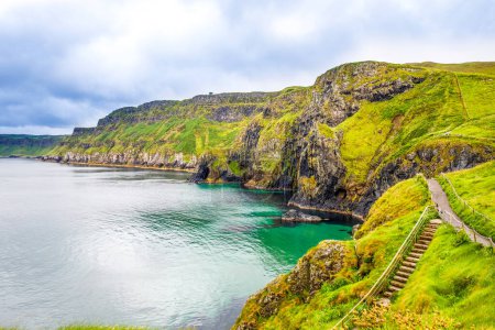 View from Carrick-a-Rede Rope Bridge, famous rope bridge near Ballintoy in County Antrim, Northern Ireland on Irish coastline. Tourist attraction, bridge to small island on cloudy day
