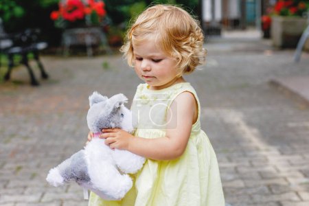 Foto de Pequeña niña jugando con un perro de juguete suave. Lindo bebé niño sosteniendo juguete y juega al aire libre - Imagen libre de derechos