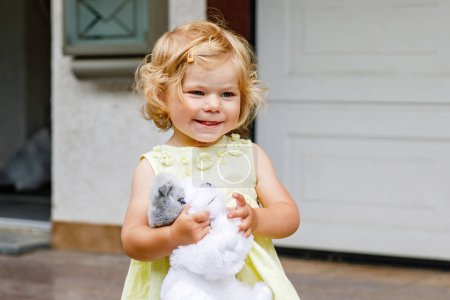 Téléchargez les photos : Petite fille tout-petit jouant avec un chien jouet mou. Mignon bébé enfant tenant jouet et joue à l'extérieur - en image libre de droit