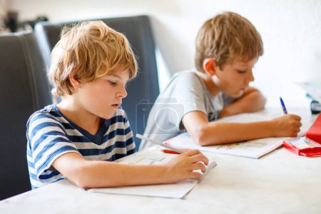 Foto de Dos chicos haciendo los deberes juntos. Hermanos, hermanos y gemelos aprendiendo en casa. Estudiantes de primaria, niños escribiendo - Imagen libre de derechos