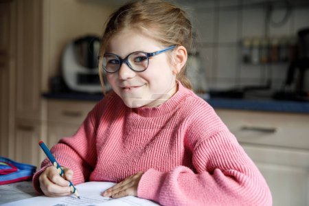 Photo for Portrait of happy little girl doing homework at home. Elementary school studing writing and learning. Smiling child writing letters, learing to write - Royalty Free Image