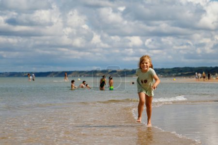 Glückliches Vorschulmädchen mit Spaß am Sandstrand Omaha an der Atlantikküste der Normandie, Frankreich. Sommeraktivitäten im Freien für Kinder.