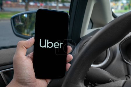 Téléchargez les photos : Chauffeur Uber tenant smartphone dans la voiture. Uber est une société américaine offrant des services de transport en ligne. Uber APP - en image libre de droit