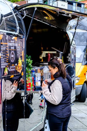 Téléchargez les photos : Stavanger, Rogaland, Norvège, 19 mai 2023, Femme debout seule par un camion-restaurant éphémère servant un comptoir en attente de nourriture - en image libre de droit