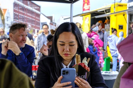 Téléchargez les photos : Stavanger, Rogaland, Norvège, 19 mai 2023, Jeune femme asiatique utilisant son téléphone portable Manger au marché de plats à emporter Stavanger - en image libre de droit