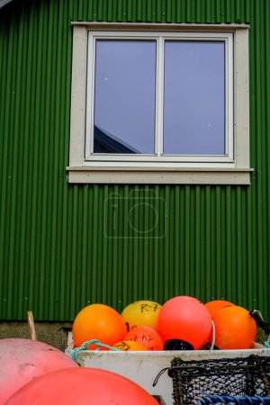 Photo for Olberg; Olbergstranden; Raege; Norway; May 20 2023, Orange Plastic Fishing Lobster Or Crab Pot Marker Buoys With Traditional Green Painted Building Behind - Royalty Free Image