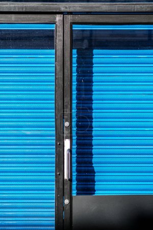 Kingston-Upon-Thames, London UK, February 12 2024,  closed Shop Protected With Bright Blue Security Shutter And Black Glazed Door With No People