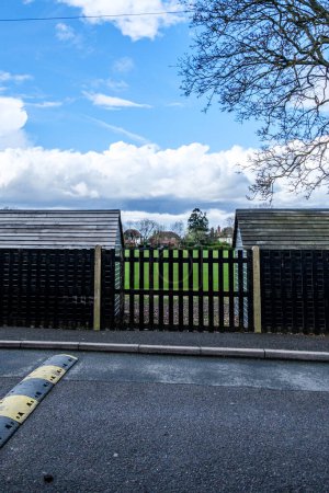 Leatherhead Surrey, UK, April 01 2024, Two Black Painted Wooden Sheds With Metal Fence And Tree In School Playing Fields With No People