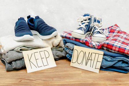 Photo for Stack of old baby children clothes,sneakers sorted into Keep and Donate categories.Donation,volunteering help,humanitarian aid.charity on gray background still life.Recycle clothing,eco cotton. - Royalty Free Image