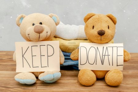 Foto de Stack of old baby children clothes,teddy bear toys,sorted into Keep and Donate categories.Donation,volunteering help,humanitarian aid.charity on gray background still life.Recycle clothing,eco cotton. - Imagen libre de derechos