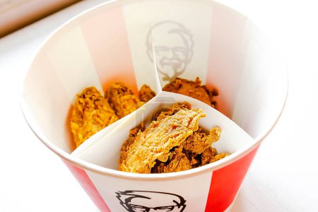 Photo for Bucket,chicken nuggets,wings,legs,Fries,coffee menu on tray in KFC restaurant.Fastfood junk food delivery,to go,takeout,take away in kraft paper eco disposable container-Kiev,Ukraine,27 December 2022 - Royalty Free Image