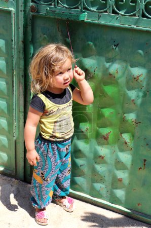 Foto de OVAKENT,ANTAKYA,TURKEY-JUNE 03:Unidentified Afghan Girl with an Apple playing with door string.June 03,2017 in Ovakent, Antakya, Turkey - Imagen libre de derechos