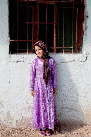 Foto de OVAKENT,HATAY,TURKEY-DECEMBER 10:Unidentified Afghan Girl in traditional Dress standing by the wall. December 10,2016 in Ovakent, Hatay, Turkey - Imagen libre de derechos