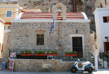 Téléchargez les photos : KALYMNOS, GRÈCE-16 JUILLET : Un scooter stationné devant la petite chapelle grecque avec drapeau grec. 16 juillet 2013 à Kalymnos, Grèce - en image libre de droit