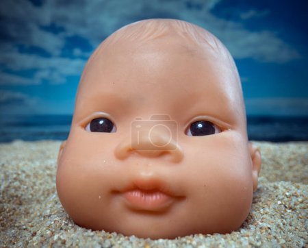 Téléchargez les photos : Une poupée de bébé à sa tête sur une plage regardant autour - en image libre de droit