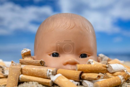 Photo for A baby doll surrounded by cigarettes on a beautiful beach - Royalty Free Image