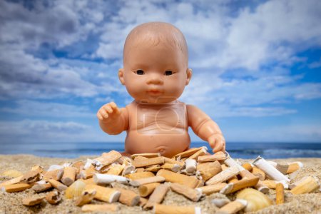 Foto de Una muñeca rodeada de cigarrillos en una hermosa playa - Imagen libre de derechos