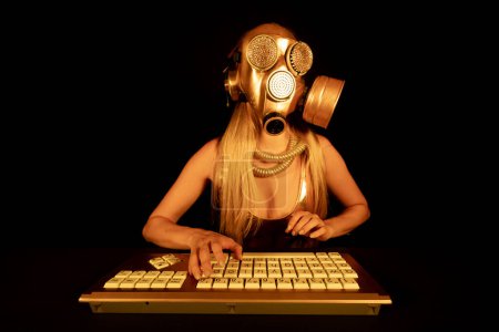 Téléchargez les photos : Une femme avec un masque à gaz doré tapant sur ordinateur - en image libre de droit
