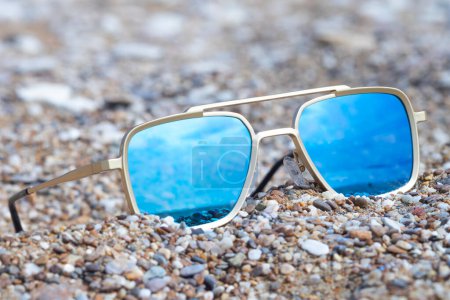 Foto de Gafas de sol espejadas en una playa que refleja el mar - Imagen libre de derechos