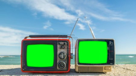 Téléchargez les photos : Téléviseurs rétro avec écran vert à côté de la mer, pour ajouter votre propre contenu sur les téléviseurs - en image libre de droit