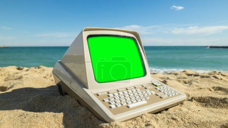 Téléchargez les photos : Ordinateur rétro sur une plage avec écran vert - en image libre de droit