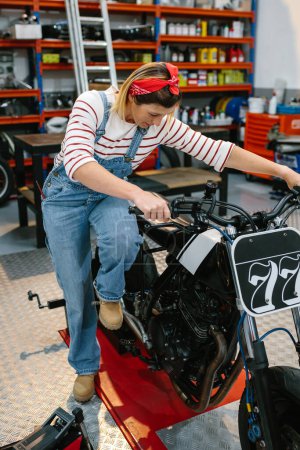 Foto de Mujer mecánica con su pie sobre el motor de arranque de arranque de arranque de la motocicleta personalizada en fábrica - Imagen libre de derechos