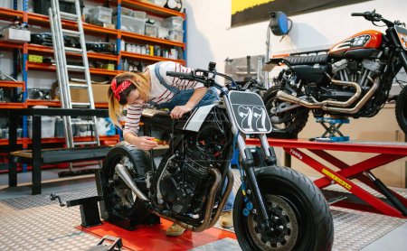 Téléchargez les photos : Mécanicien femme avec tournevis réparer moto personnalisée sur la plate-forme sur l'usine - en image libre de droit