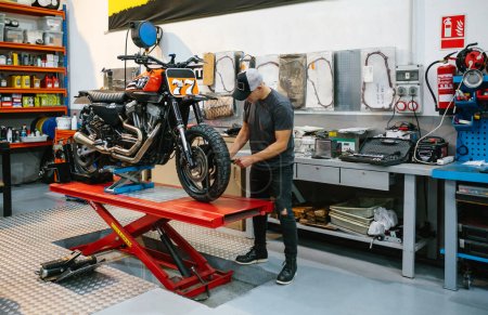 Foto de Hombre mecánico irreconocible que comprueba el motor de la motocicleta personalizada sobre la plataforma en fábrica - Imagen libre de derechos