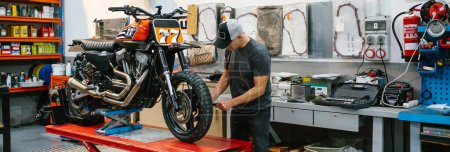 Unrecognizable mechanic man checking engine of custom motorcycle over platform on factory