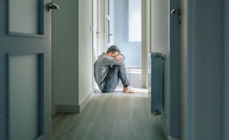 Foto de Hombre irreconocible con trastorno mental y pensamientos suicidas llorando sentado en el suelo del pasillo - Imagen libre de derechos