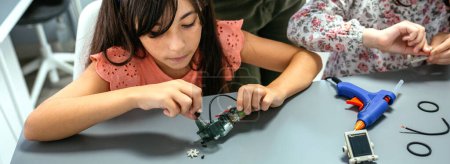 Téléchargez les photos : Étudiante concentrée vissant un circuit électrique à côté d'un écolier dans une classe de robotique. Concept d'éducation technologique élémentaire. - en image libre de droit