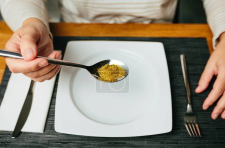 Close up of unrecognizable woman ready to eat holding a spoon full of golden glitter composed of plastics harmful to humans and environment. Concept about of European Union ban use of microplastics.