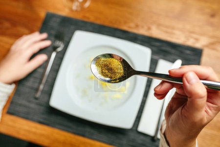 Unrecognizable woman hand holding a spoon full of golden glitter composed of plastics harmful to humans and environment. Concept about risks of eating food contaminated with microplastics.