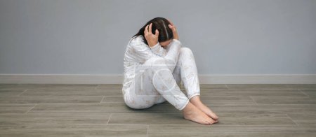 Foto de Mujer irreconocible con trastorno mental y pensamientos suicidas sosteniendo su cabeza con las manos sentadas en el suelo - Imagen libre de derechos